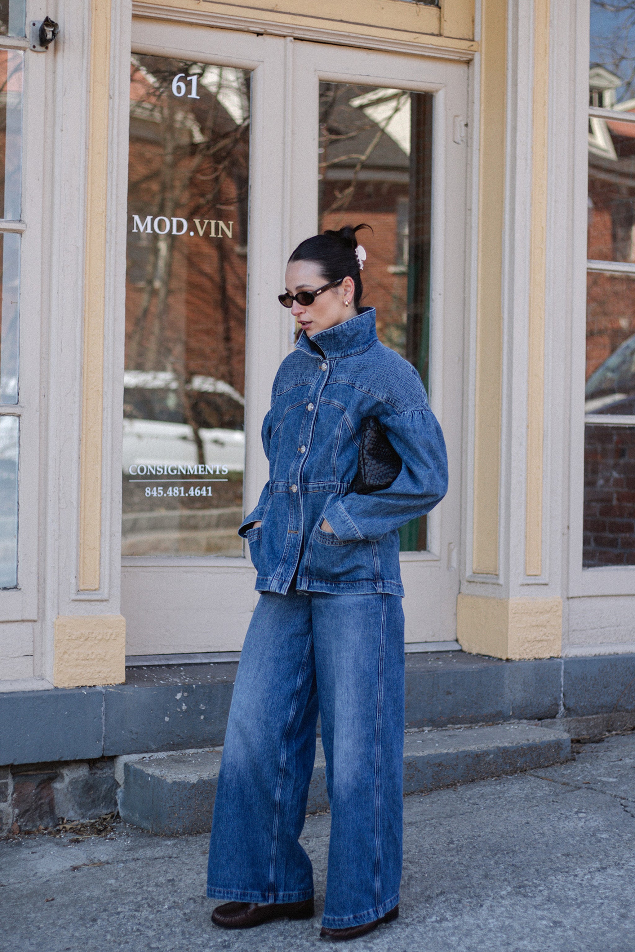 Woman wearing a denim jacket and blue wide leg jeans infront of a glass doorway