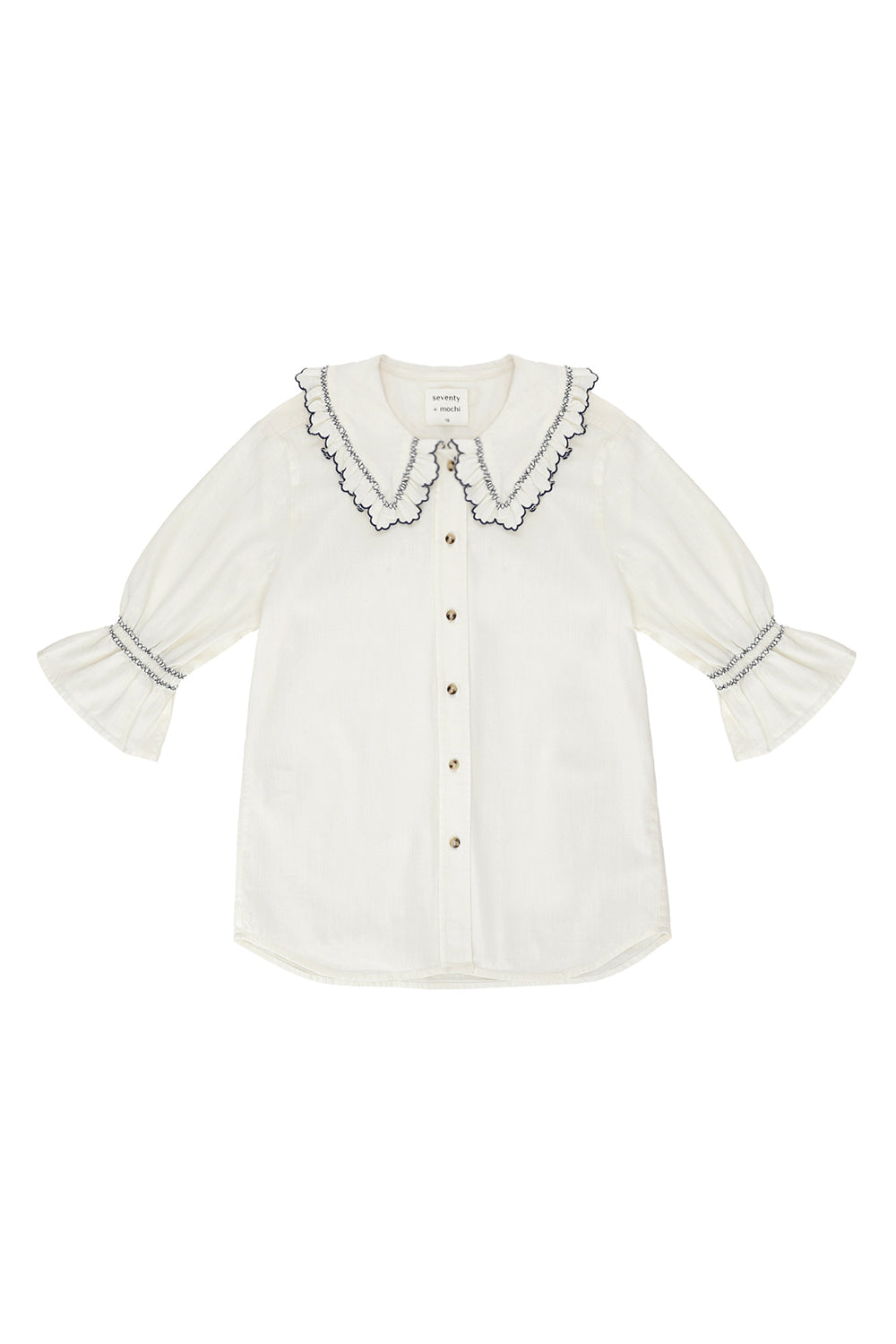 A white organic cotton blouse with dark blue embroiderery on frilled sleeves and a frill peek-a-boo collar on a white background