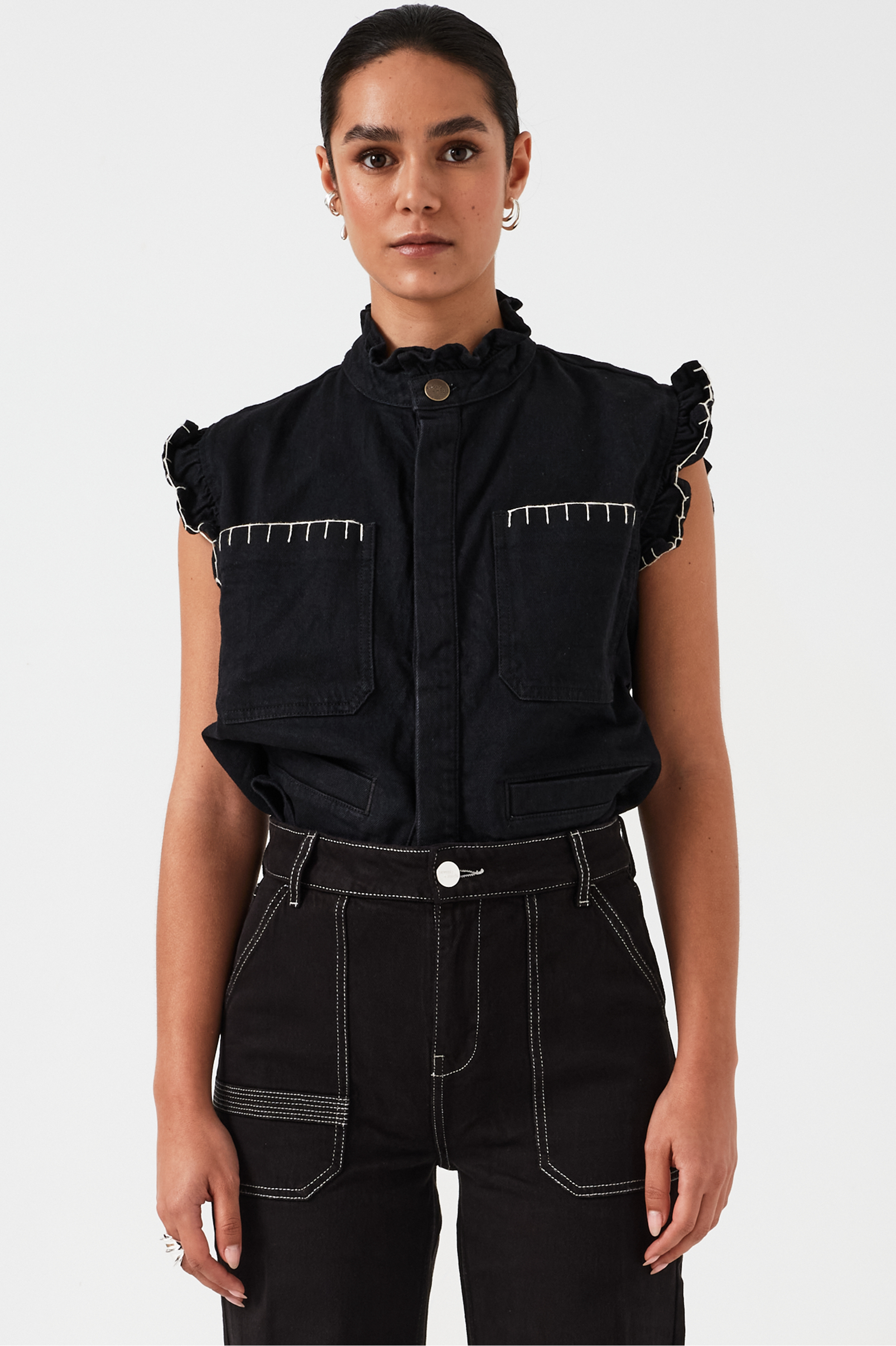 woman wearing a black vest/ waistcoat with a frill collar and our signature white stitching on two large patch pockets, paired with black jeans against a white backdrop