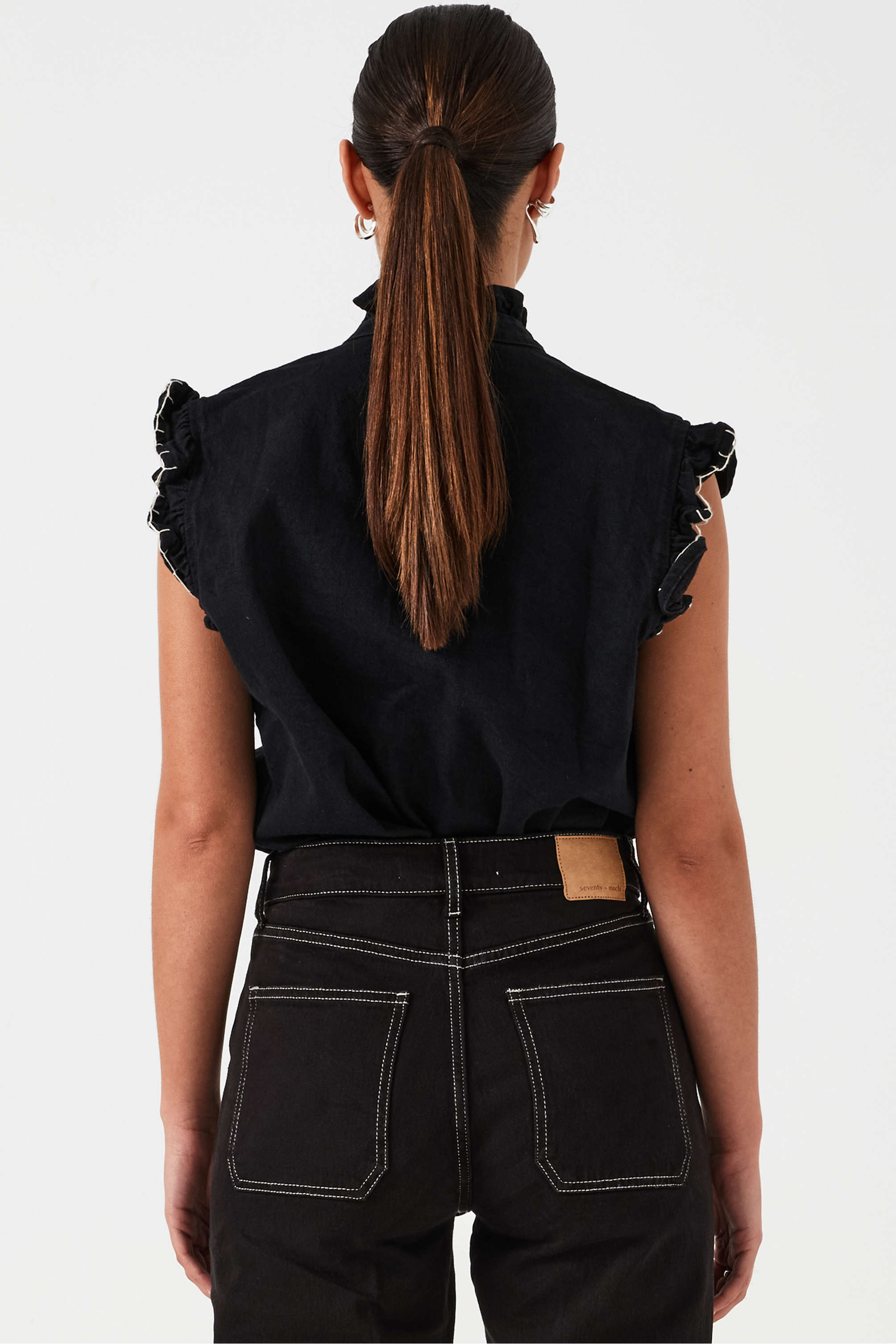 woman wearing a black vest/ waistcoat with a frill collar and our signature white stitching on two large patch pockets, paired with black jeans against a white backdrop