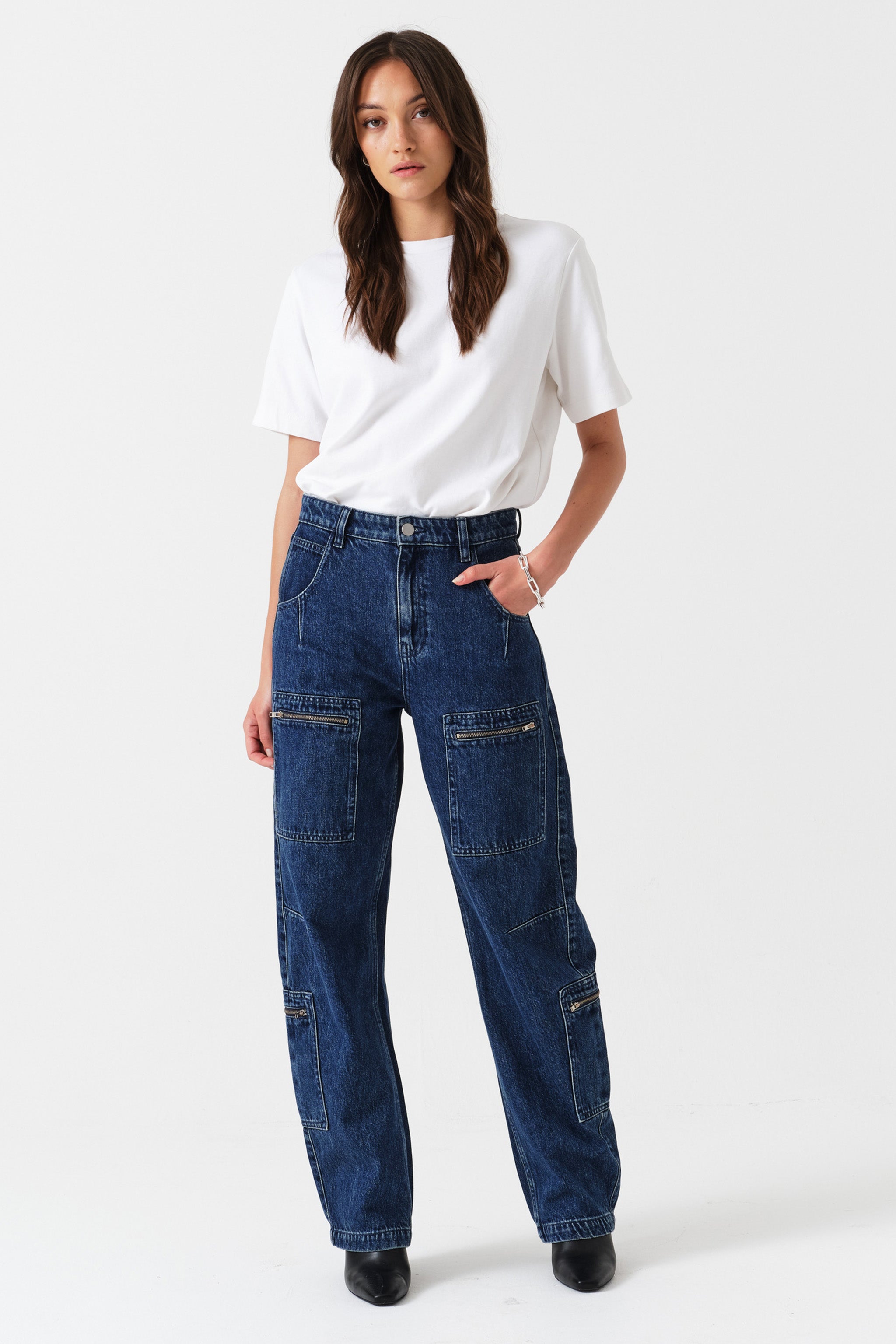 Woman wearing a white t-shirt and blue jeans with cargo pockets and zip details on a white background
