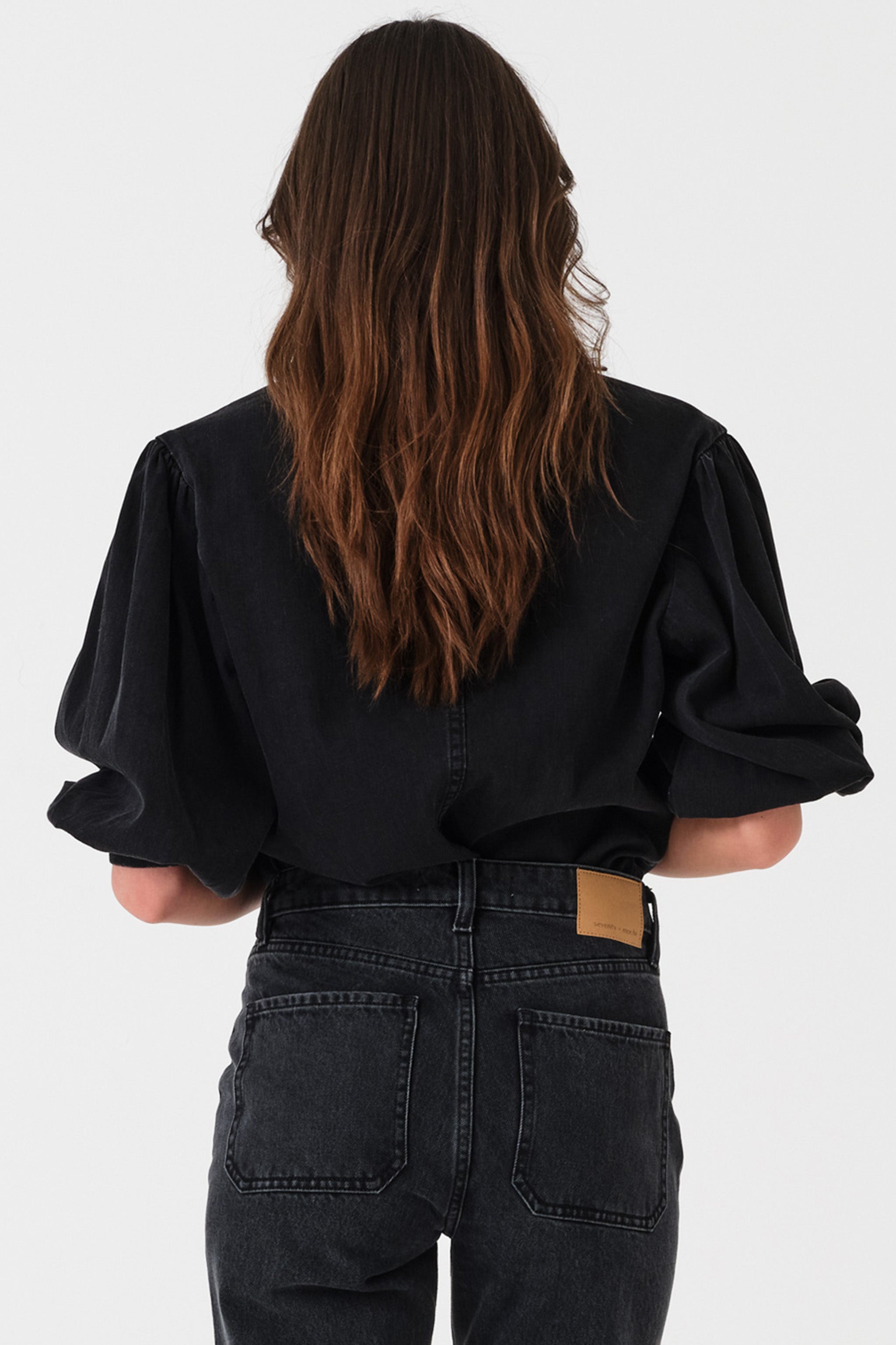 Woman showing the back of a black denim shirt with oversized collar on a white background
