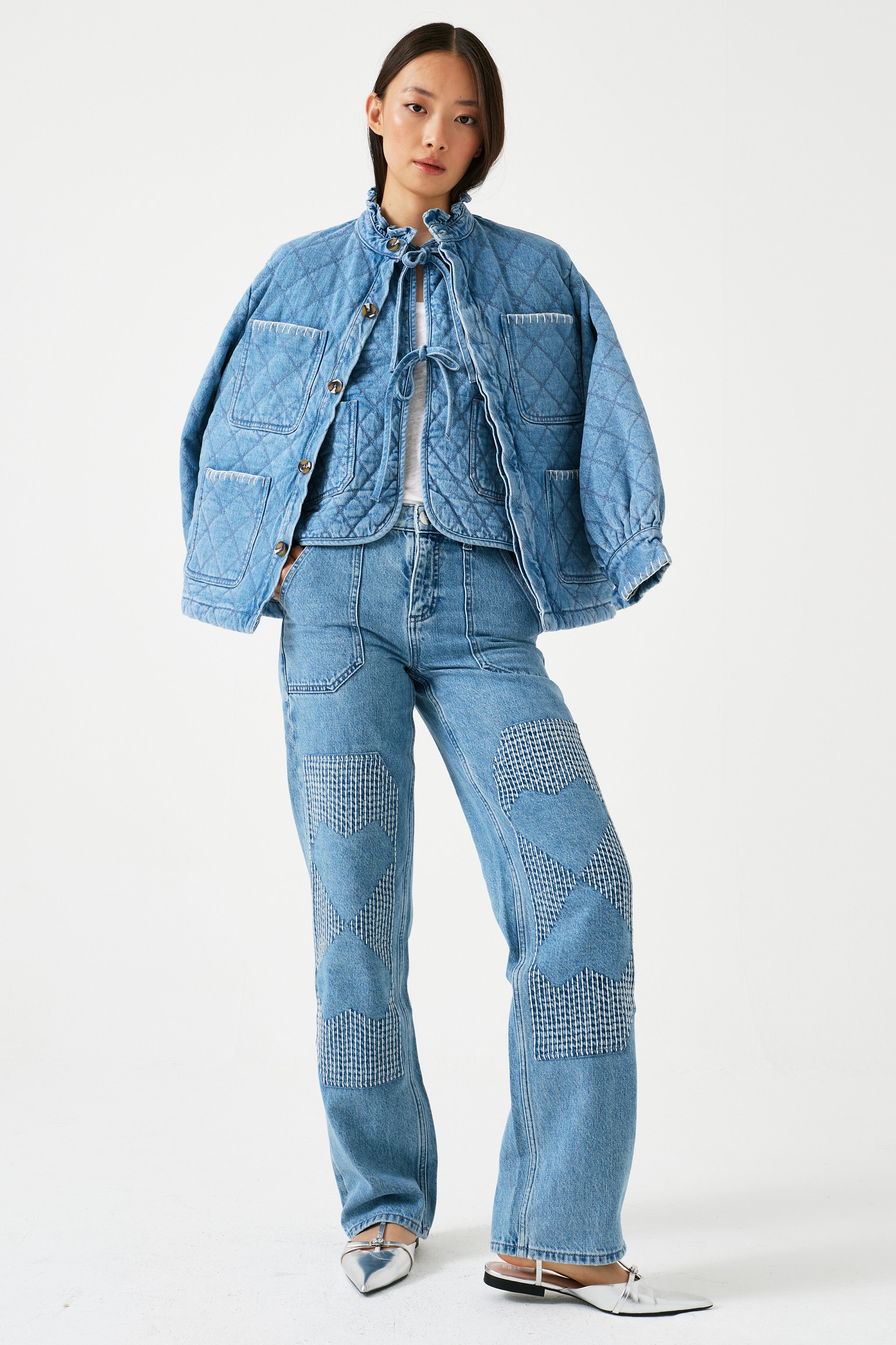 Woman wearing a blue denim outfit with a quilted denim jacket and jeans on a white background