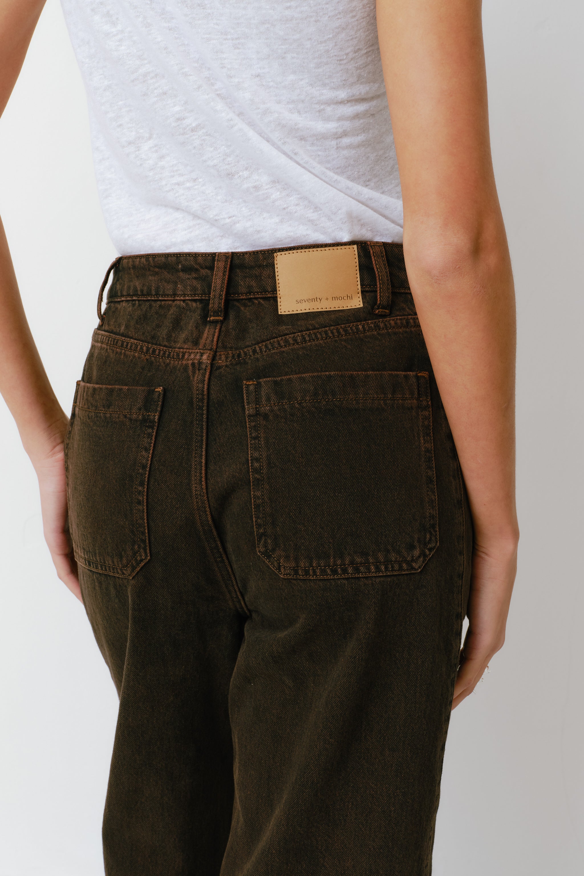 woman standing against a white background wearing high-rise dark brown cacao-colored carpenter barrel leg jeans and a white top.