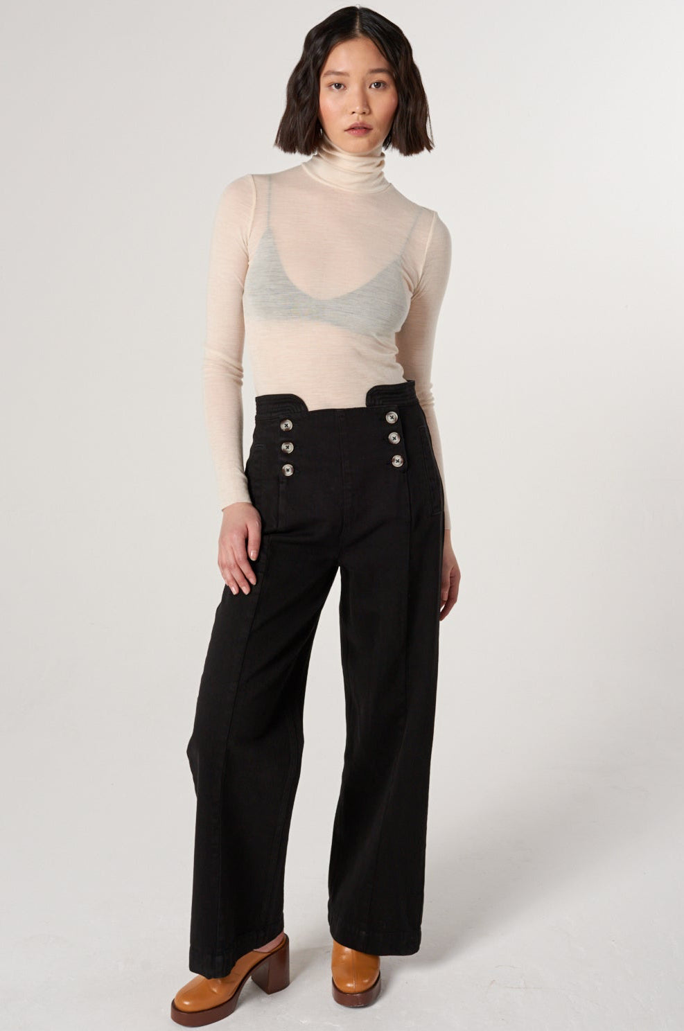 woman a white shirt and black high rise, wide leg jeans with a sailor button front fastening detail against a white backdrop