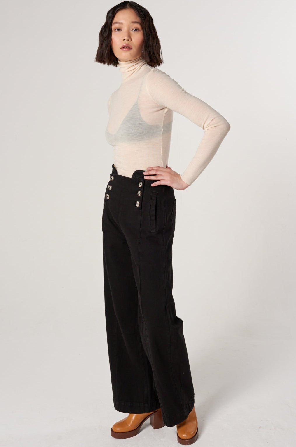 woman a white shirt and black high rise, wide leg jeans with a sailor button front fastening detail against a white backdrop