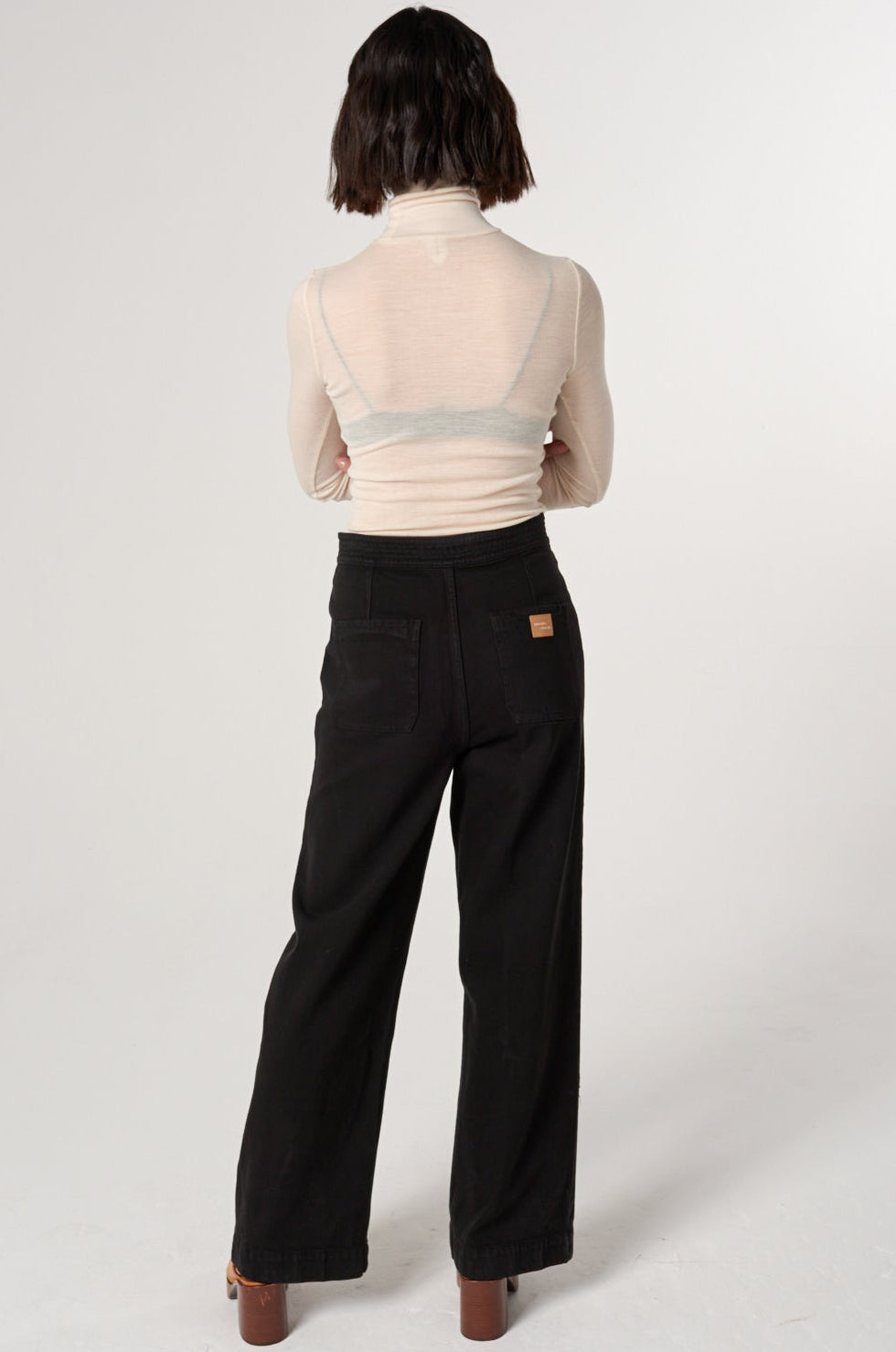 woman a white shirt and black high rise, wide leg jeans with a sailor button front fastening detail against a white backdrop