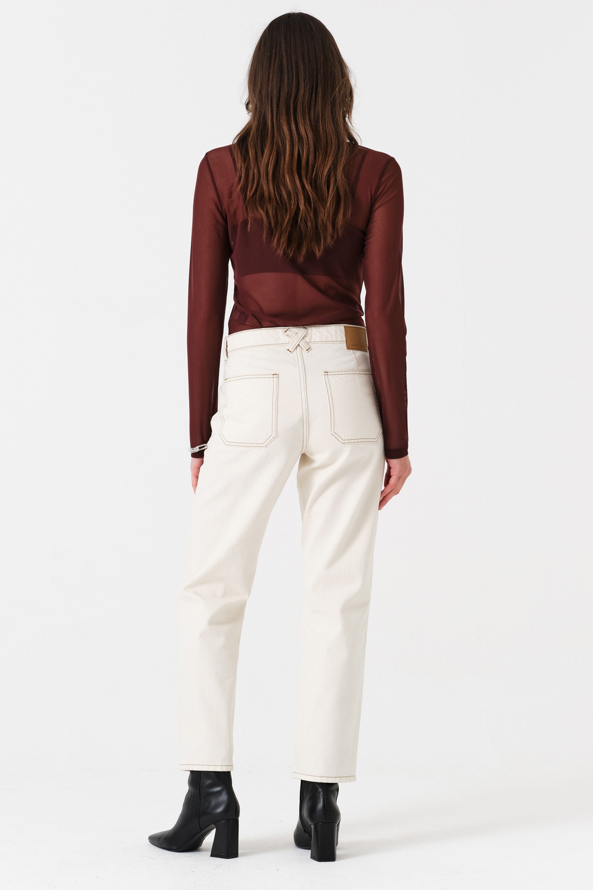 Woman wearing off white straight leg jeans and a brown shirt on a white background, photographed from the back