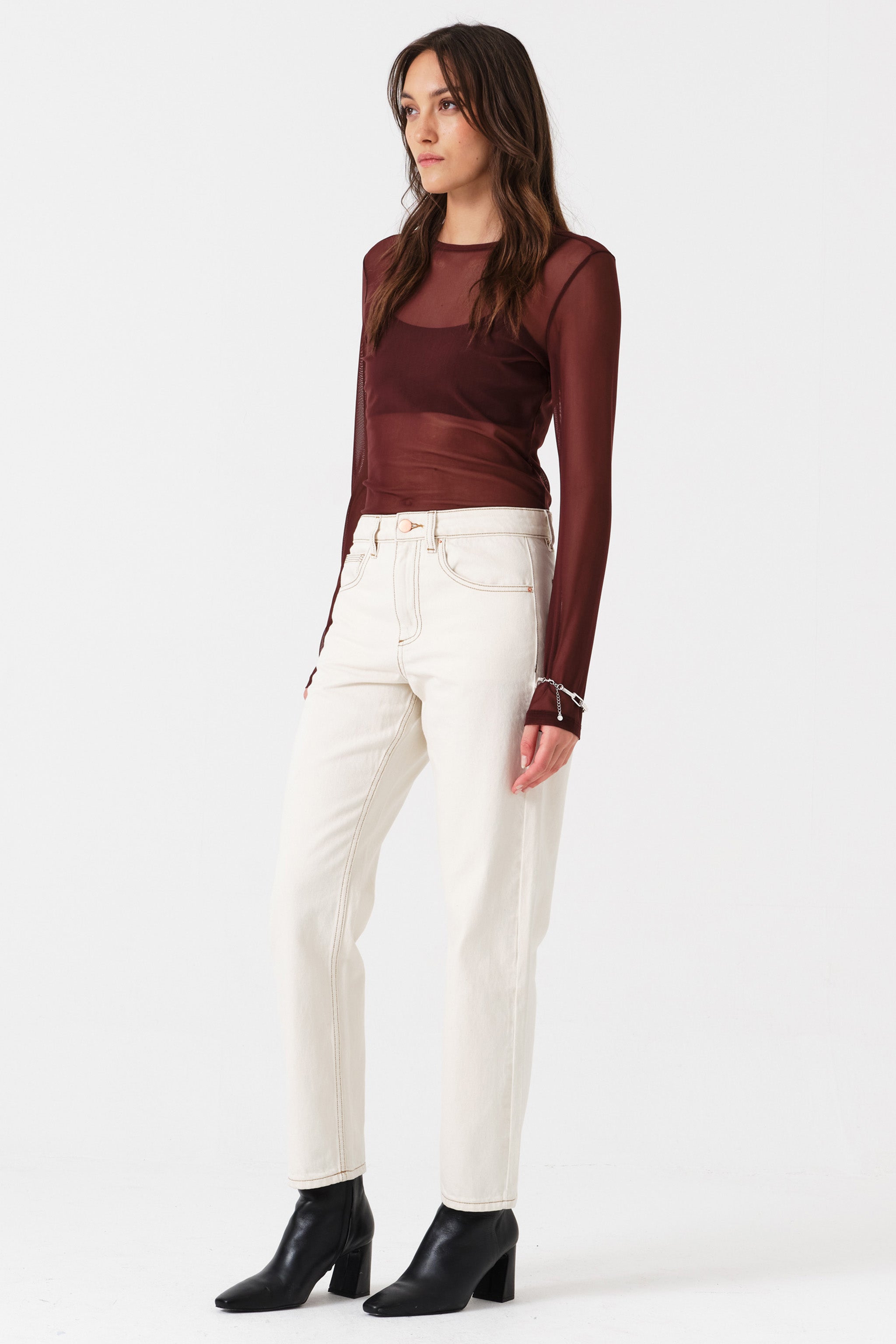 Woman wearing off white straight leg jeans and a brown shirt on a white background