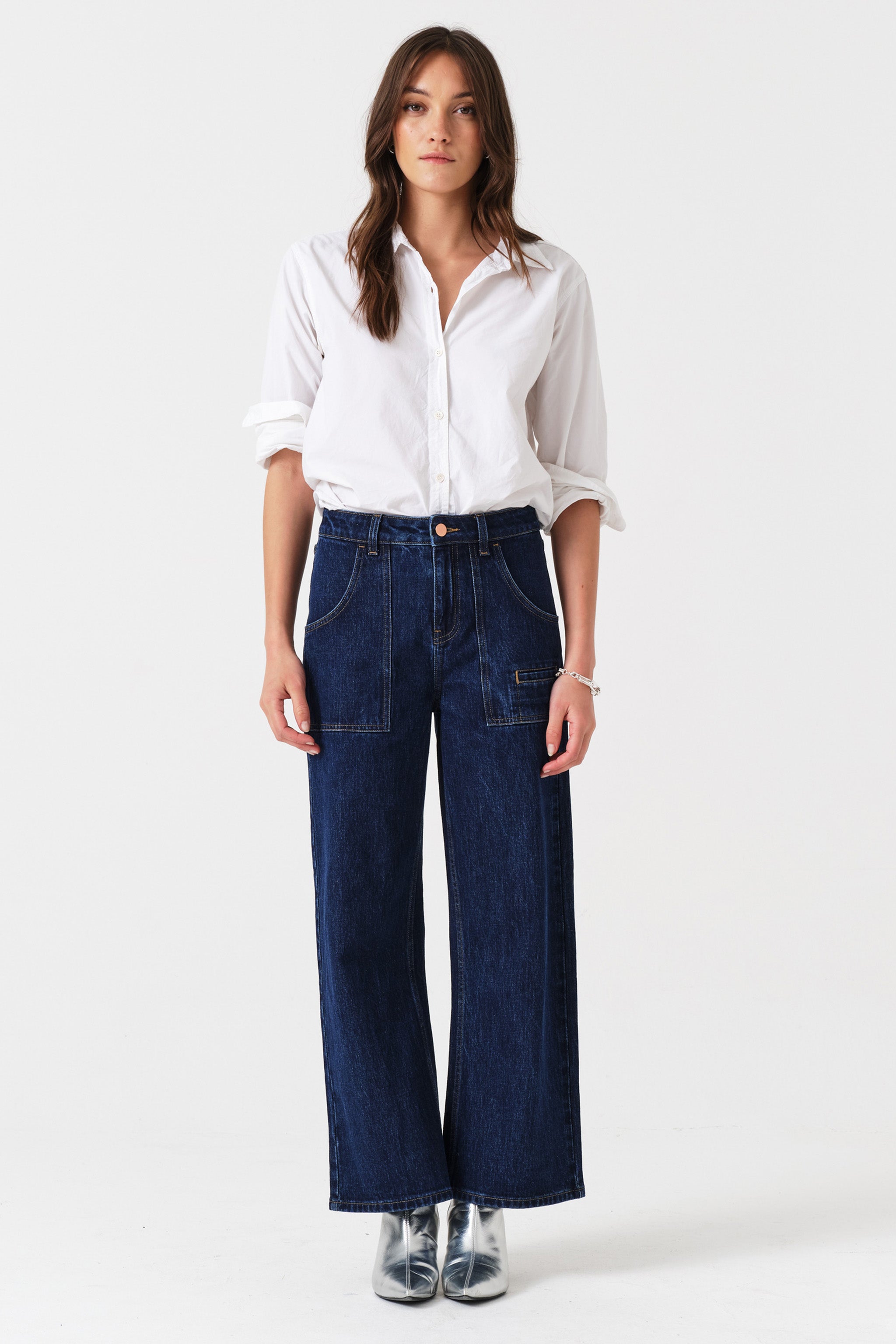 Woman wearing dark wash blue cropped wide-leg jeans with pocket details and a white shirt on a white background