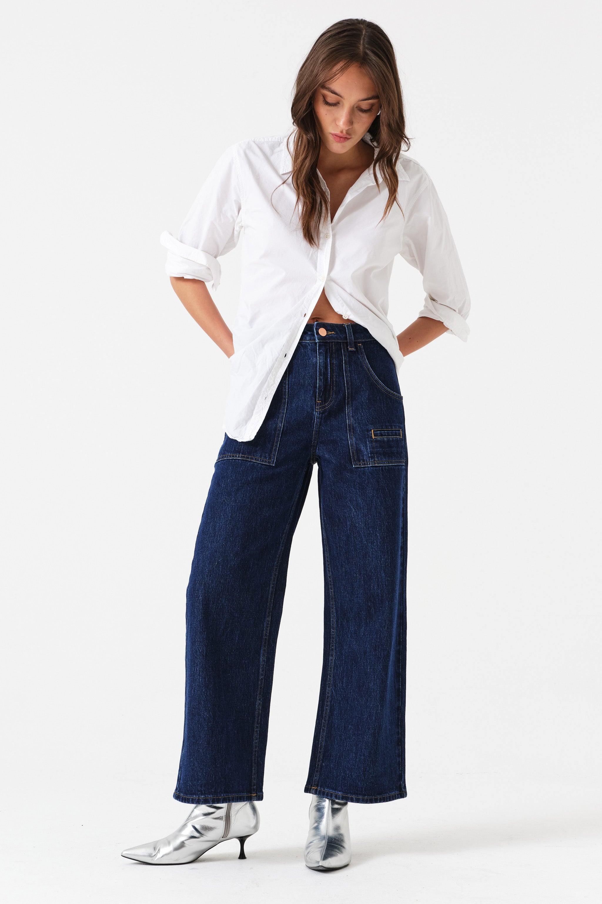 Woman wearing dark wash blue cropped wide-leg jeans with pocket details and a white shirt on a white background