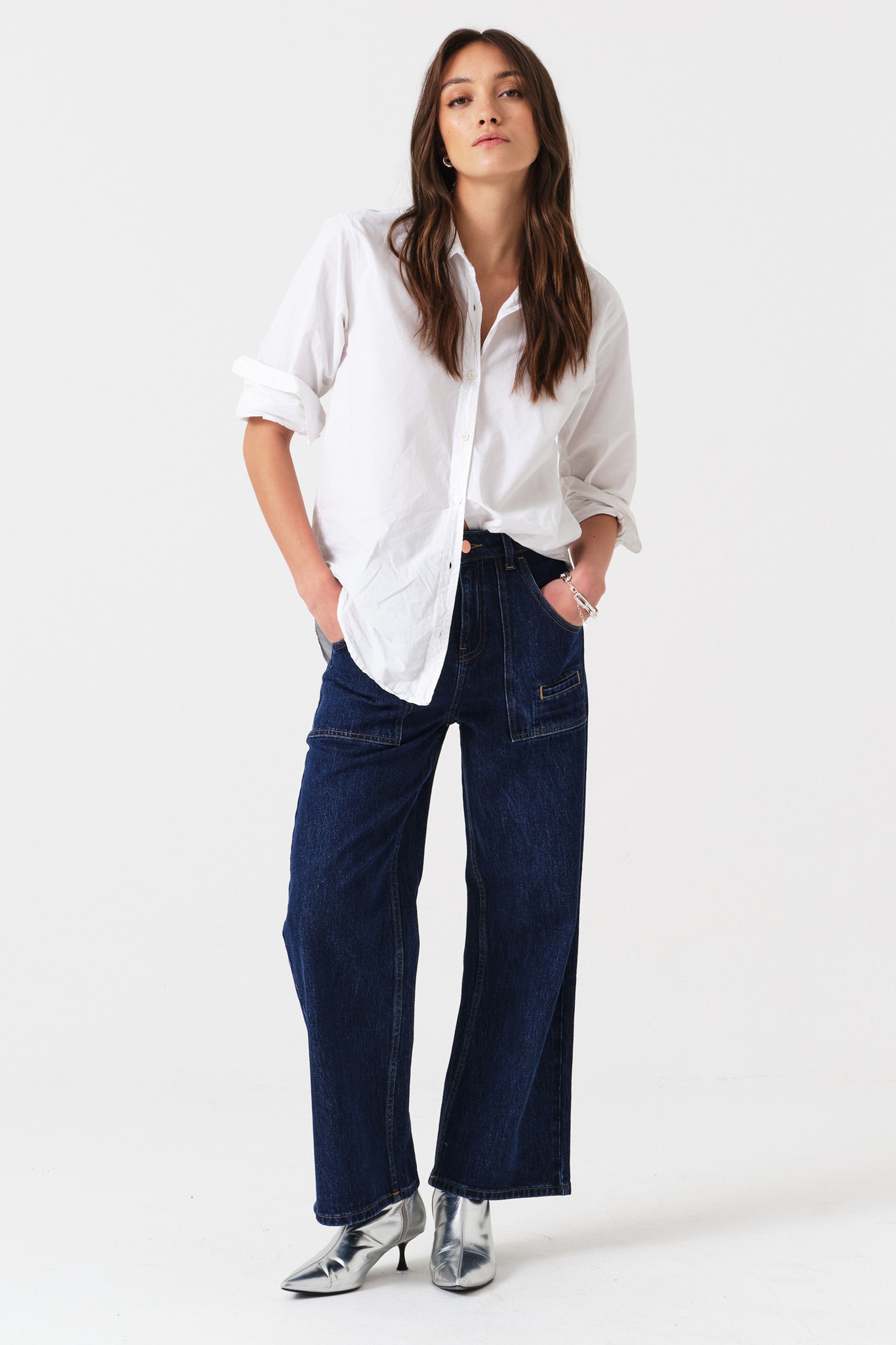 Woman wearing dark wash blue cropped wide-leg jeans with pocket details and a white shirt on a white background