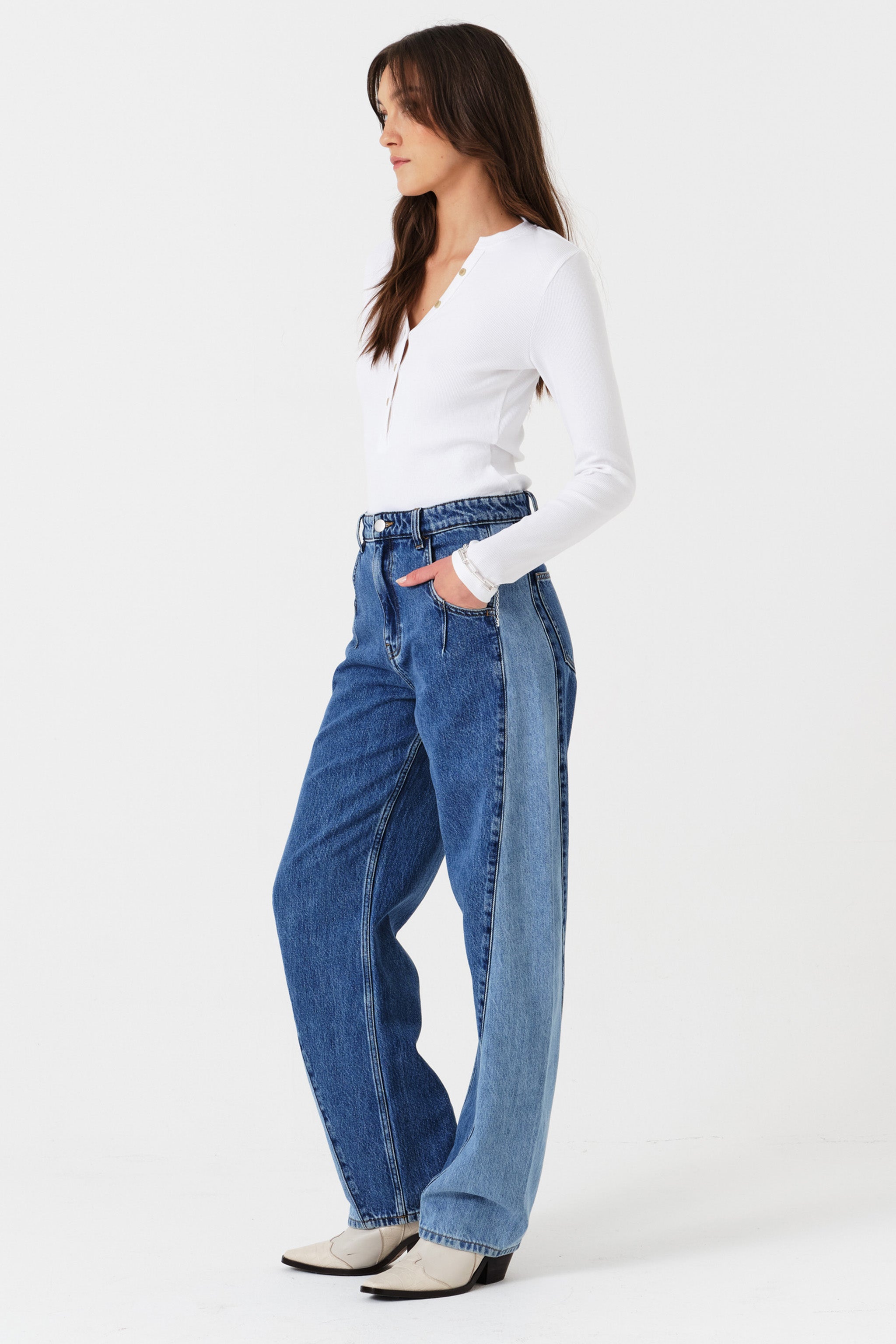 Woman wearing two toned blue barrel leg jeans and a white shirt on a white background phtoographed from the side