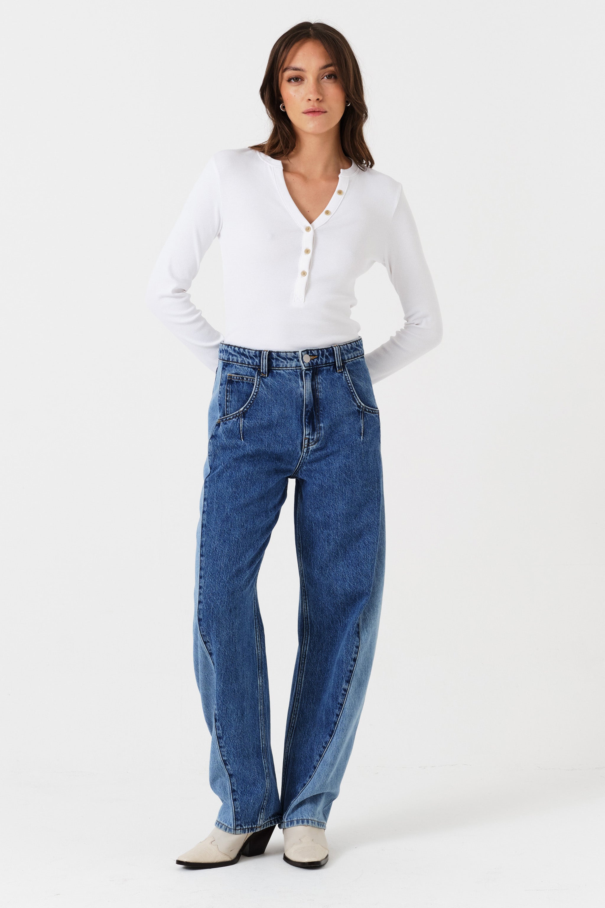 Woman wearing two toned blue barrel leg jeans and a white shirt on a white background