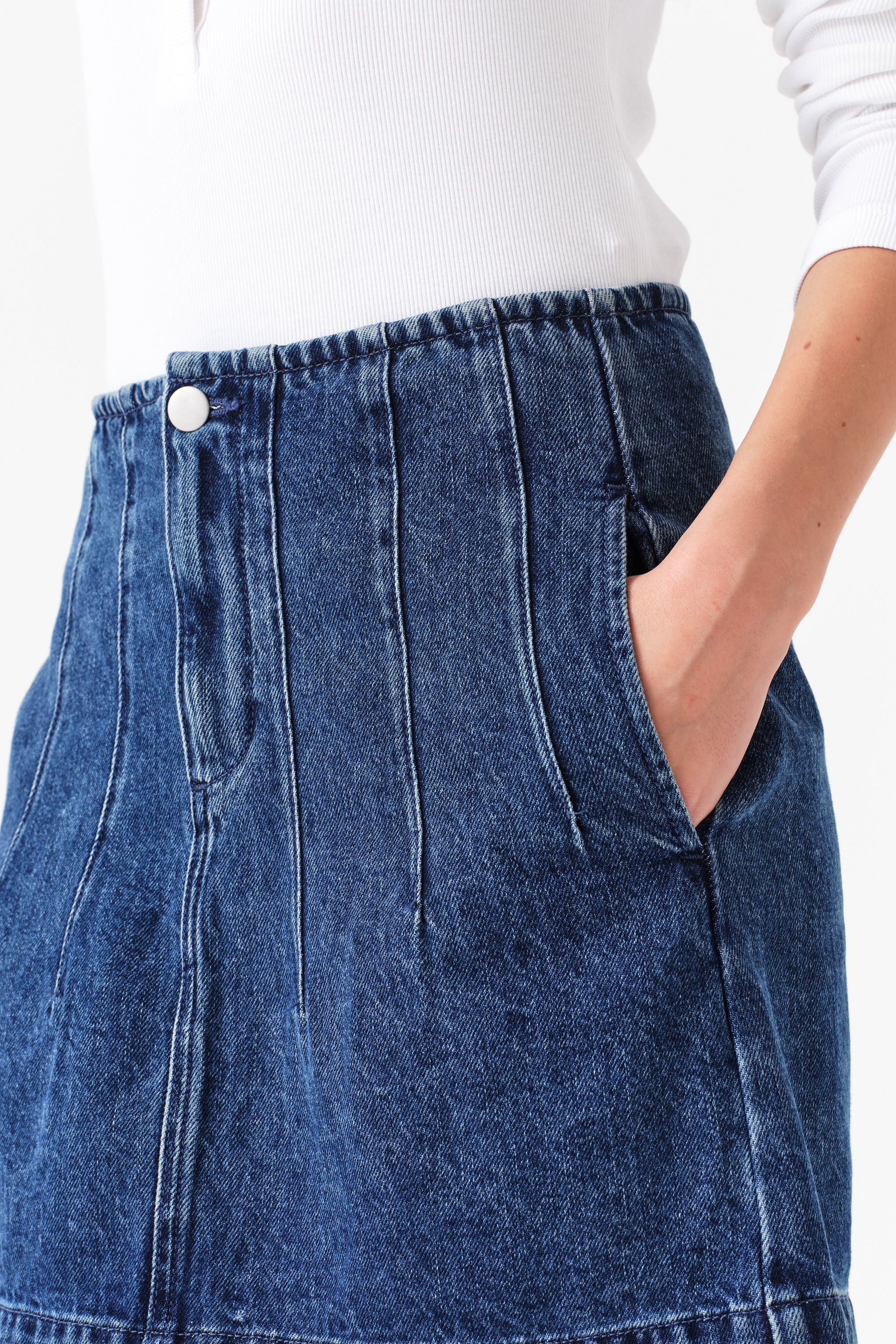 Close up of woman wearing a dark blue denim mini skirt with seam details and a white shirt on a white background