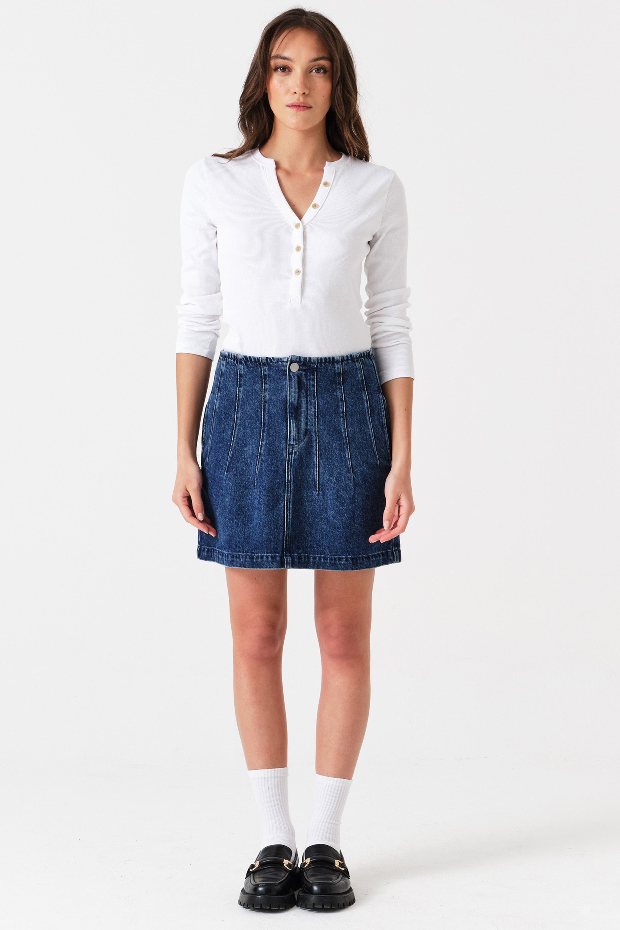 Woman wearing a dark blue denim mini skirt with seam details and a white shirt on a white background