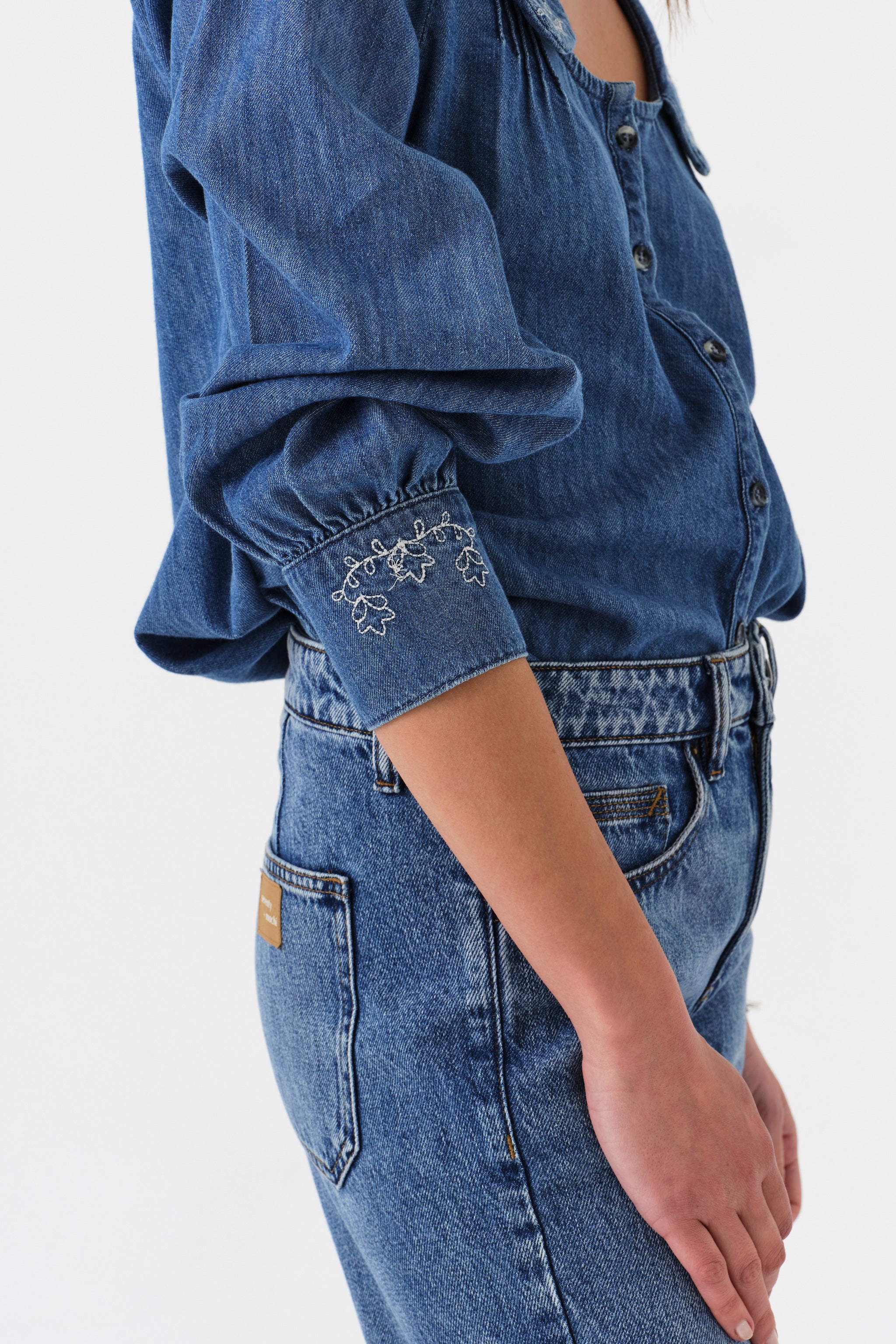 Woman wearing a blue denim blouse with embroidered details and jeans on a white background