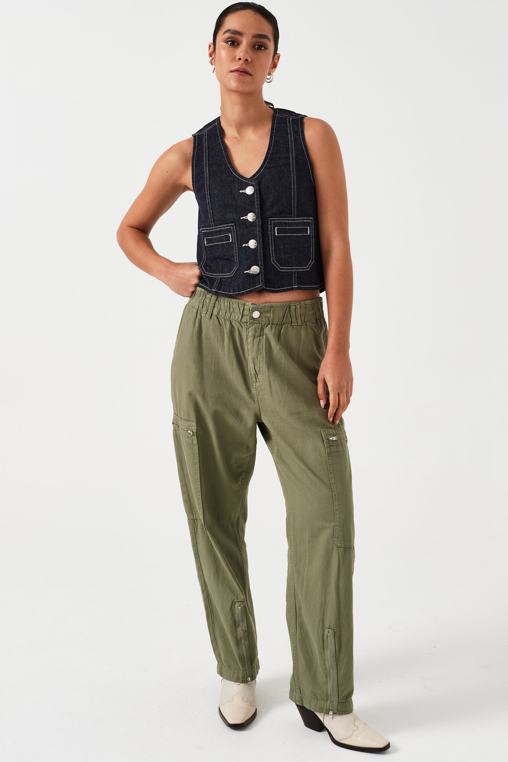 woman standing wearing lightweight cargo style khaki pants with deep zip pockets and an elastic waist and a denim vest on a white background