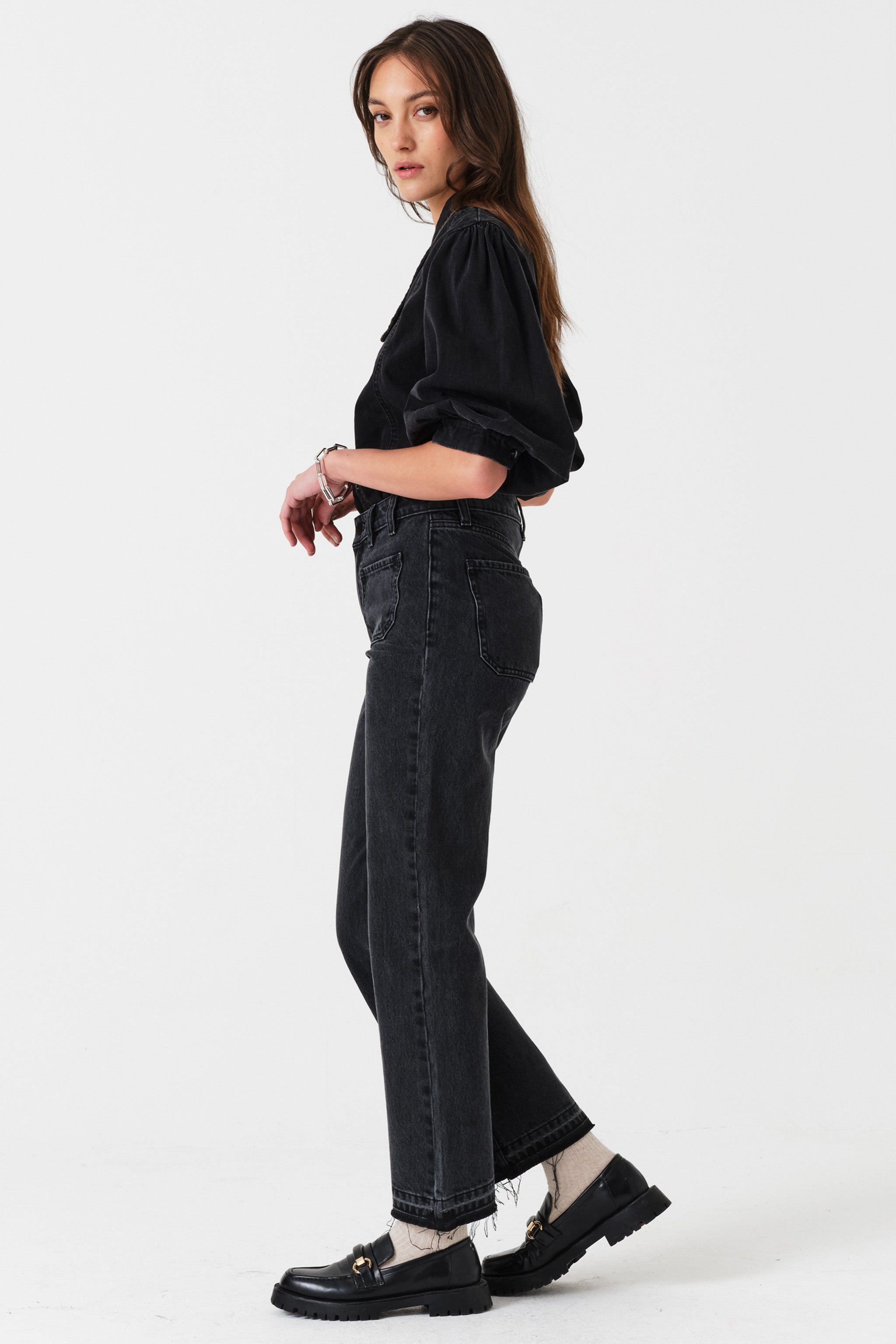 Woman showing the side of a black denim button up shirt paired with washed black jeans