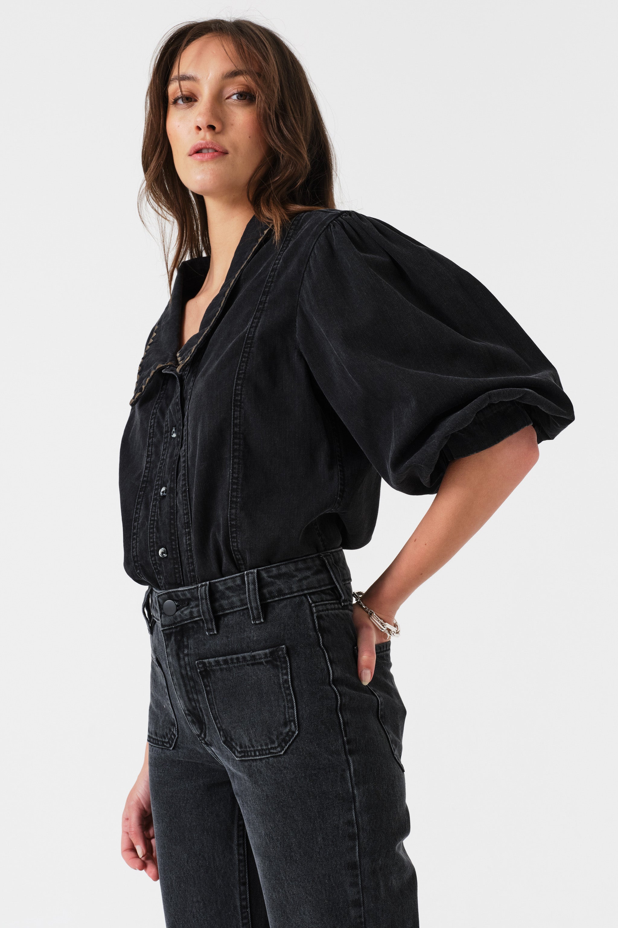 Woman wearing a black denim shirt and jeans on a white background