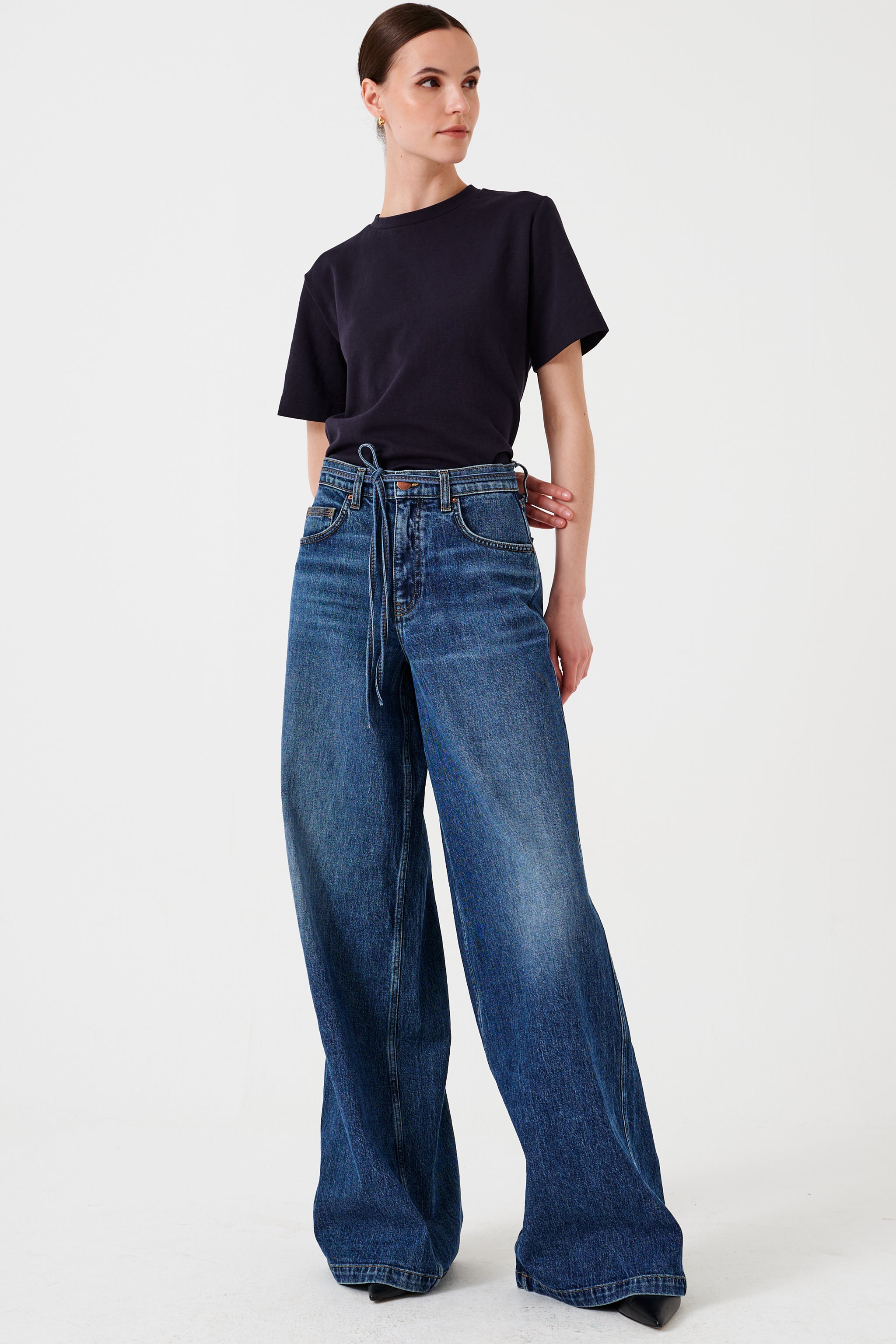 Woman wearing a black t-shirt and blue wide-leg jeans with a tie waist string detail on a white background