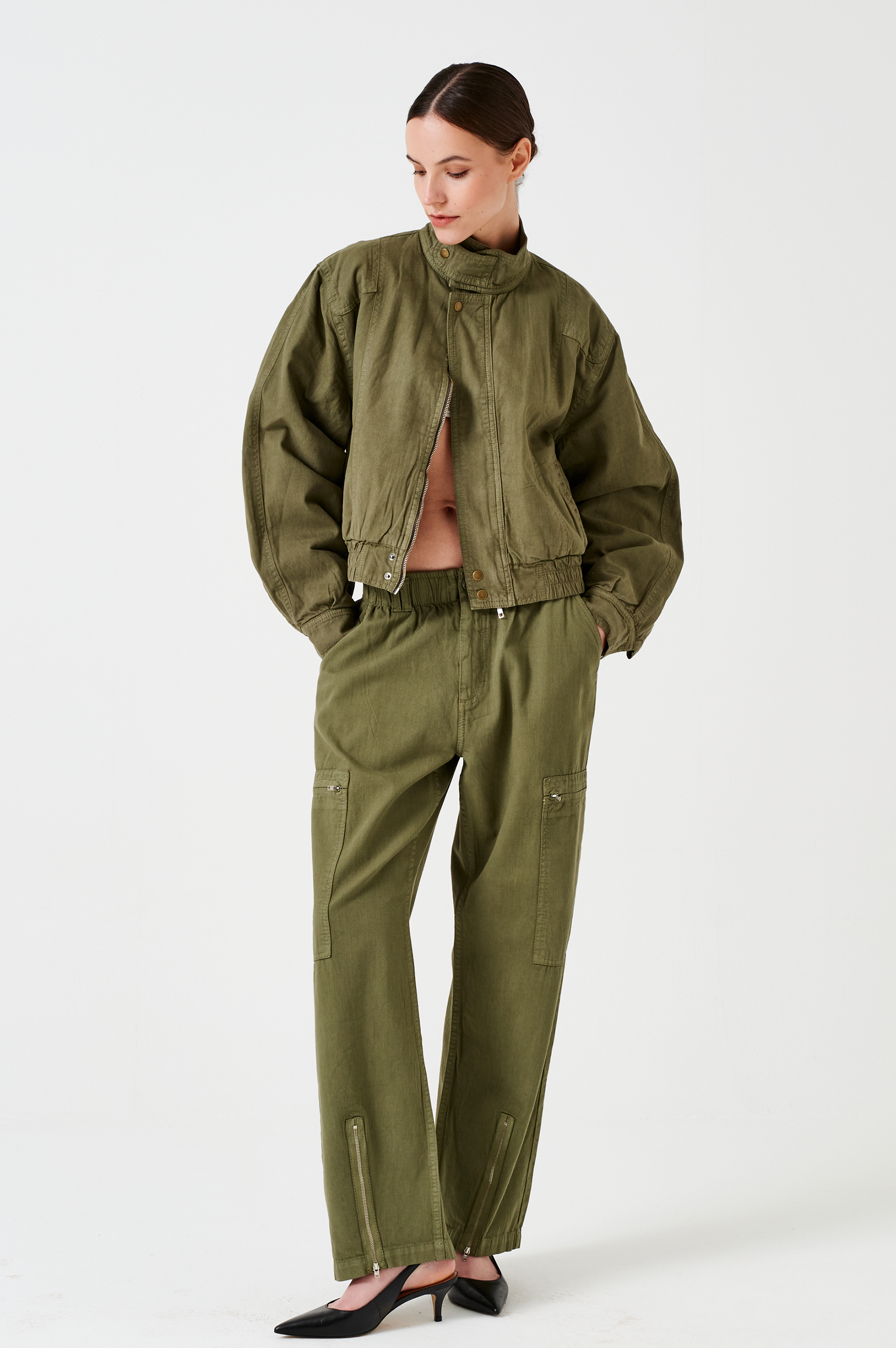 woman standing wearing lightweight cargo style khaki pants with deep zip pockets and an elastic waist and khaki bomber jacket on a white background