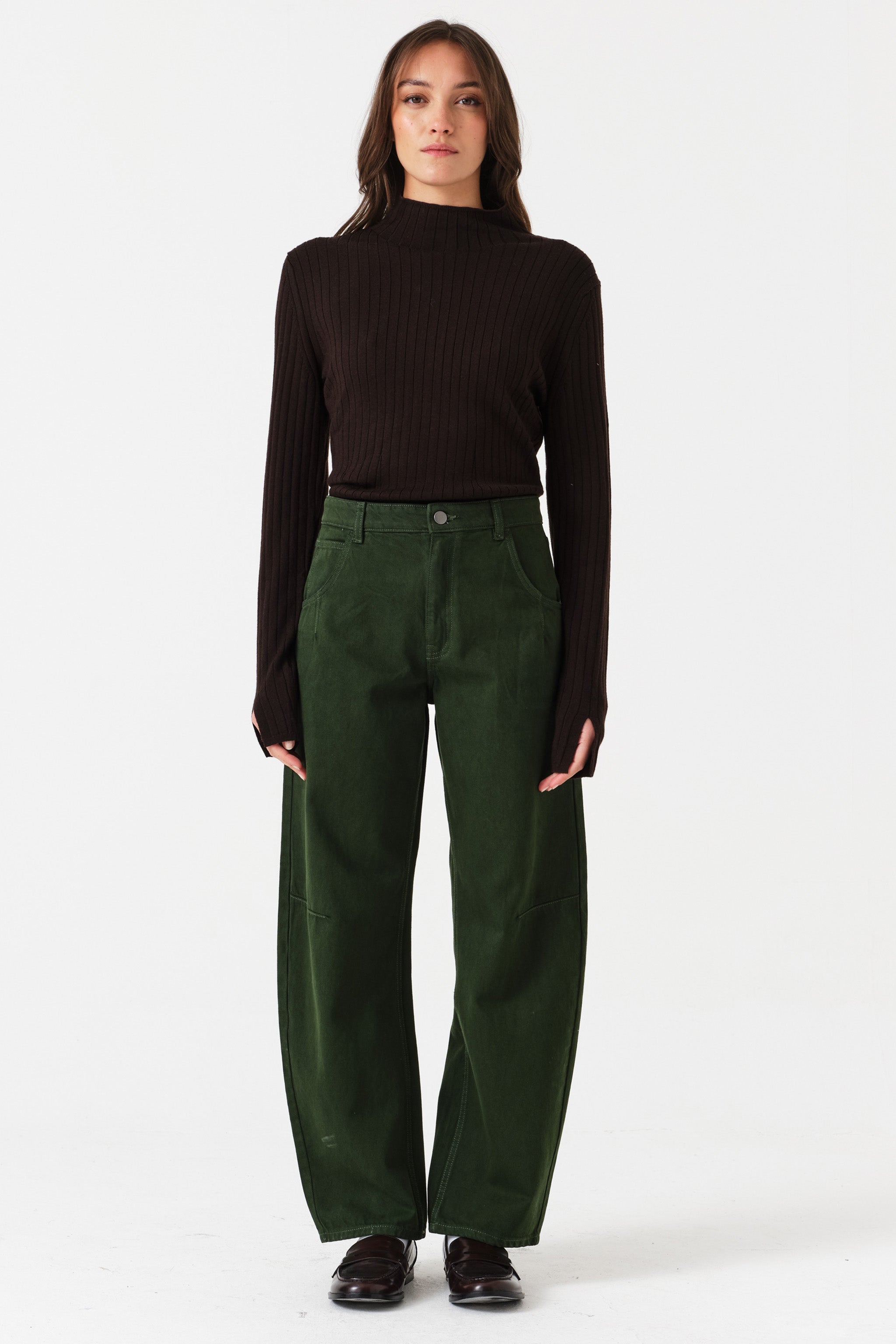 Woman wearing dark green barrel leg jeans and a brown shirt on a white background