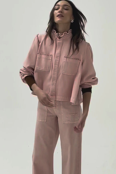 woman wearing light pink high waisted, wide, cropped jeans with big pockets, a pink shirt, and brown shoes on a white background